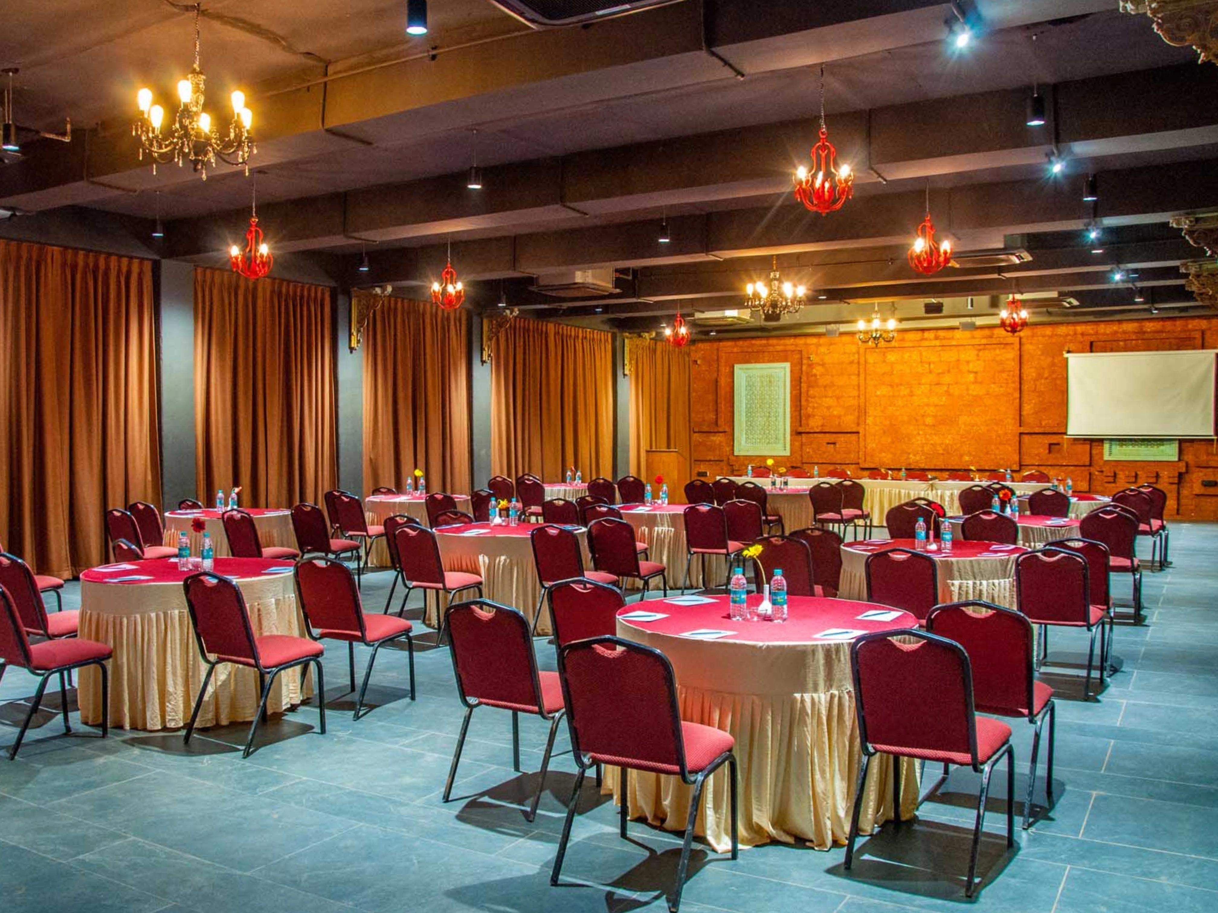 Red and black-themed indoor wedding hall with round tables and stylish lighting at Ramsukh Resort, Mahabaleshwar.